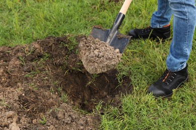 Photo of Worker digging soil with shovel outdoors, closeup