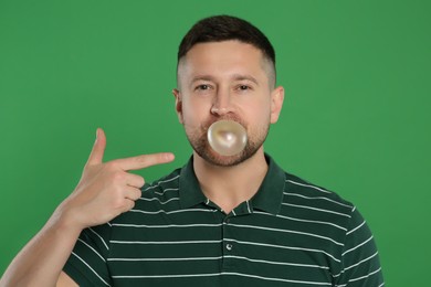 Photo of Handsome man blowing bubble gum on green background