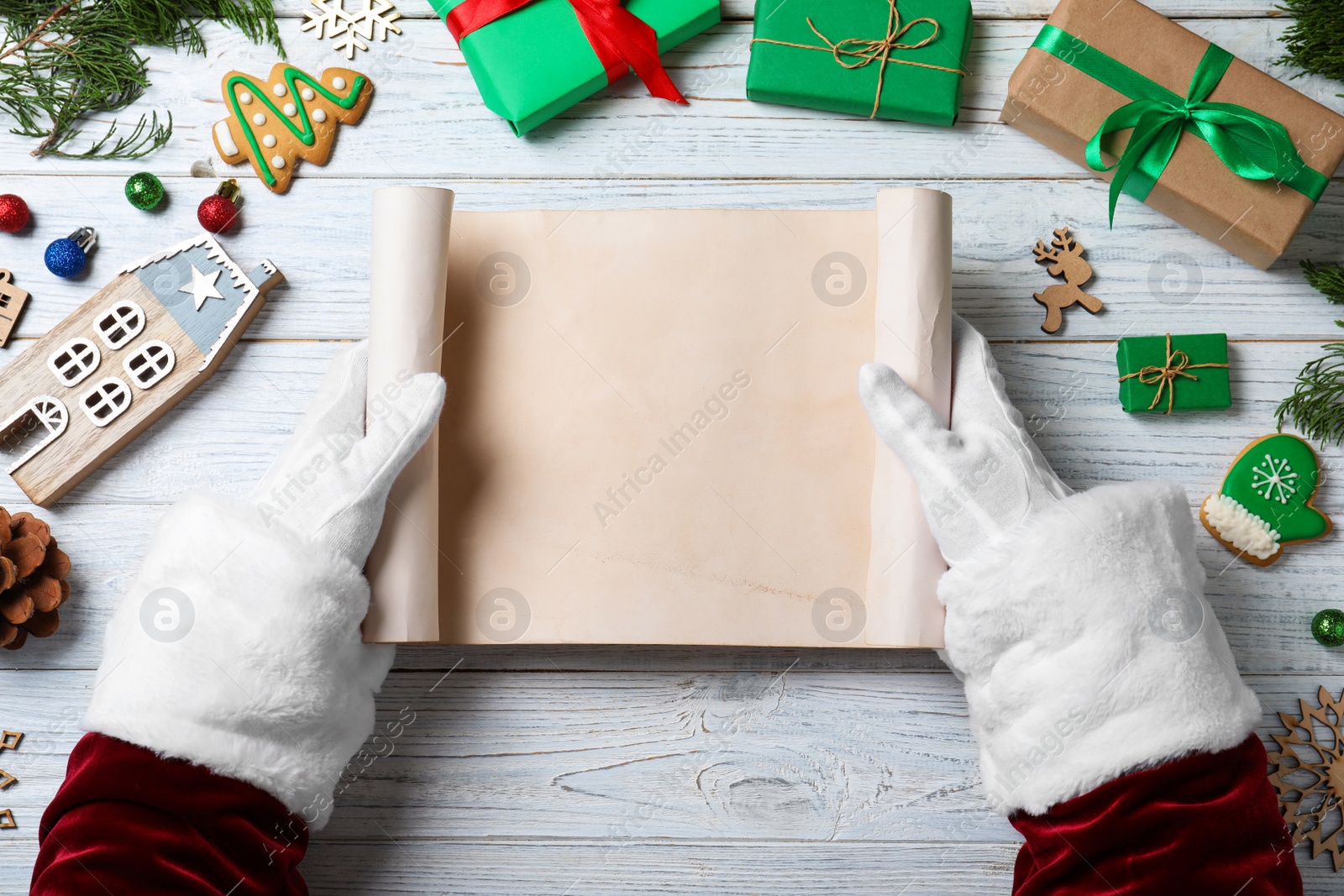 Photo of Santa Claus holding empty paper at white wooden table, top view. Space for text