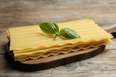 Uncooked lasagna sheets with basil on wooden table, closeup