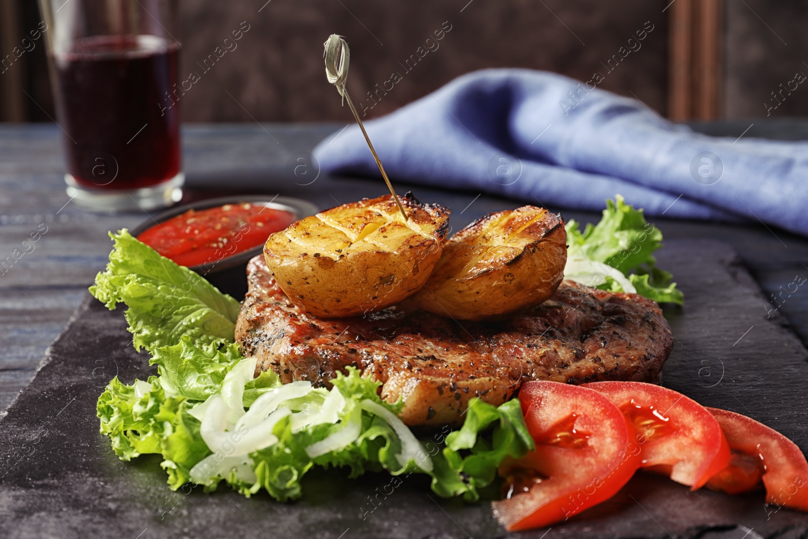 Photo of Tasty grilled meat and potatoes served on slate plate, closeup