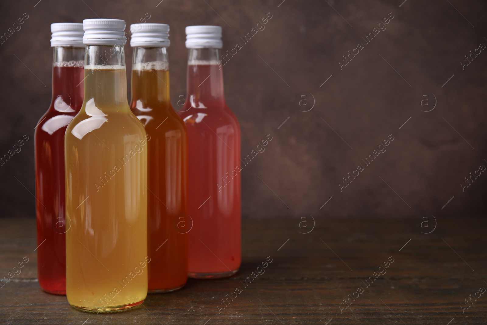 Photo of Delicious kombucha in glass bottles on wooden table, space for text