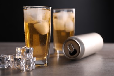 Photo of Energy drink in glasses, aluminium can and ice cubes on grey table, closeup