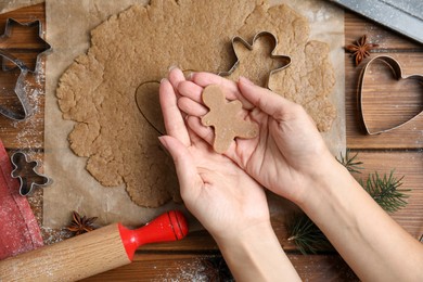 Photo of Woman holding gingerbread man over wooden table, top view. Homemade Christmas cookies