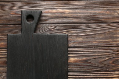 Black cutting board on wooden table, top view. Space for text