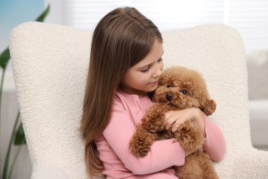 Little child with cute puppy in armchair indoors. Lovely pet