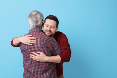 Happy son and his dad hugging on light blue background, space for text