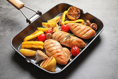 Grill pan with fried chicken breasts and garnish on grey background