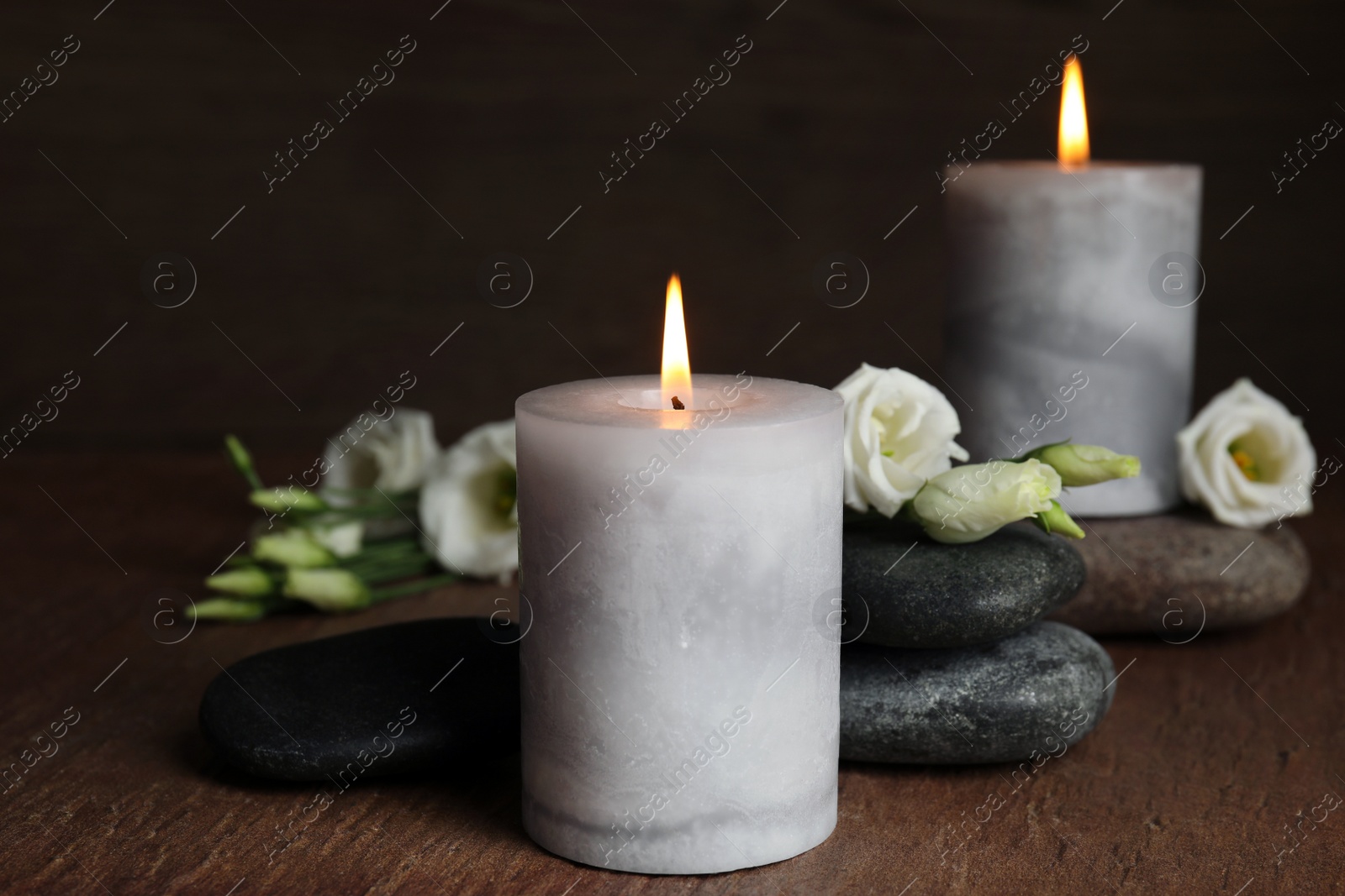 Photo of Burning candles, spa stones and flowers on wooden table