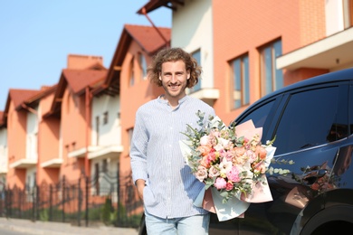 Photo of Young handsome man with beautiful flower bouquet near car on street