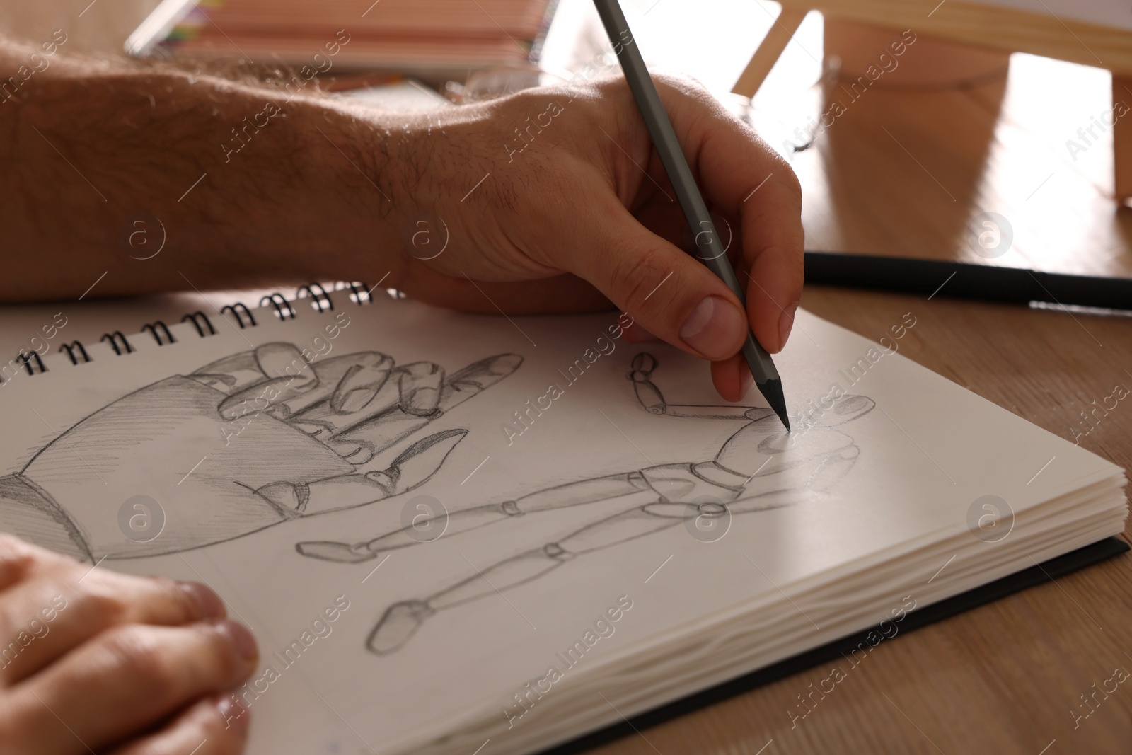 Photo of Man drawing in sketchbook with pencil at wooden table, closeup