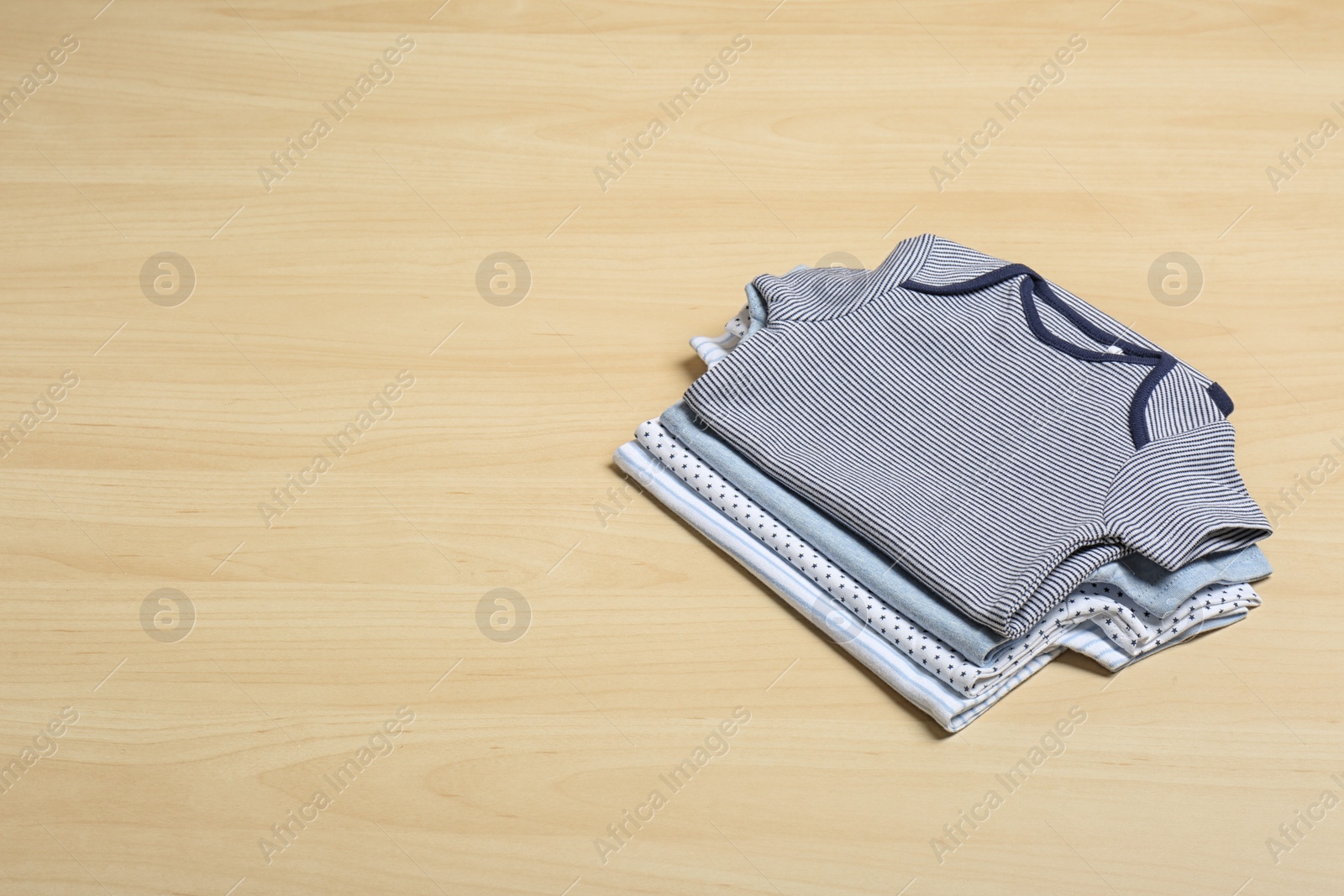 Photo of Different baby bodysuits on wooden background, space for text