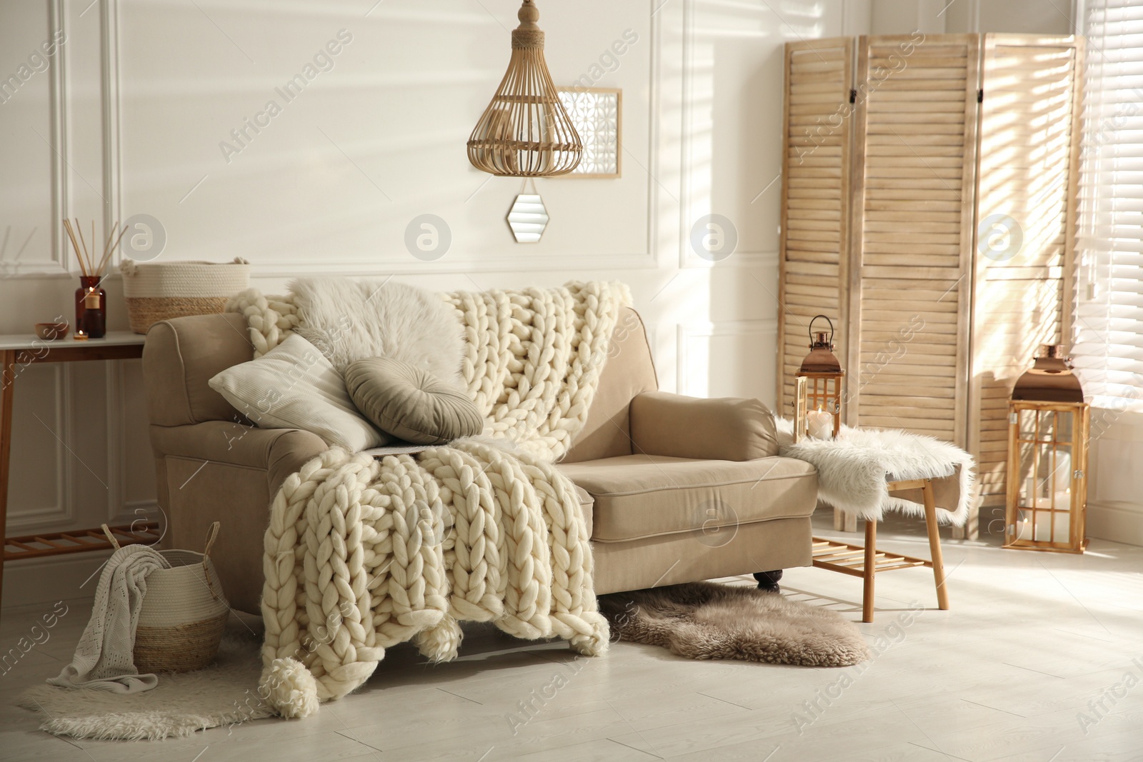 Photo of Cozy living room interior with beige sofa, knitted blanket and cushions