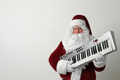 Photo of Santa Claus with synthesizer on light background, space for text. Christmas music