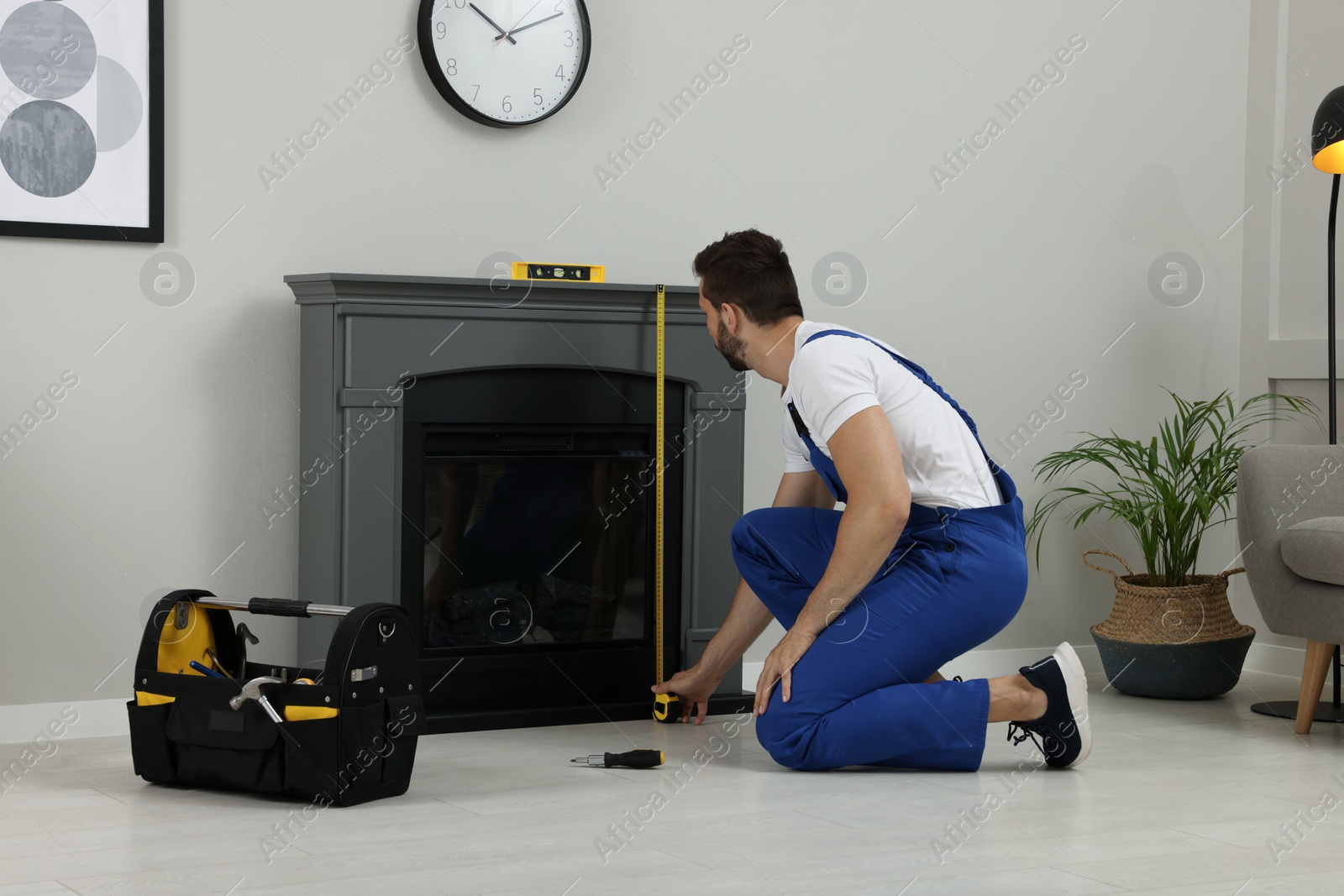 Photo of Professional technician with measuring tape installing electric fireplace in room