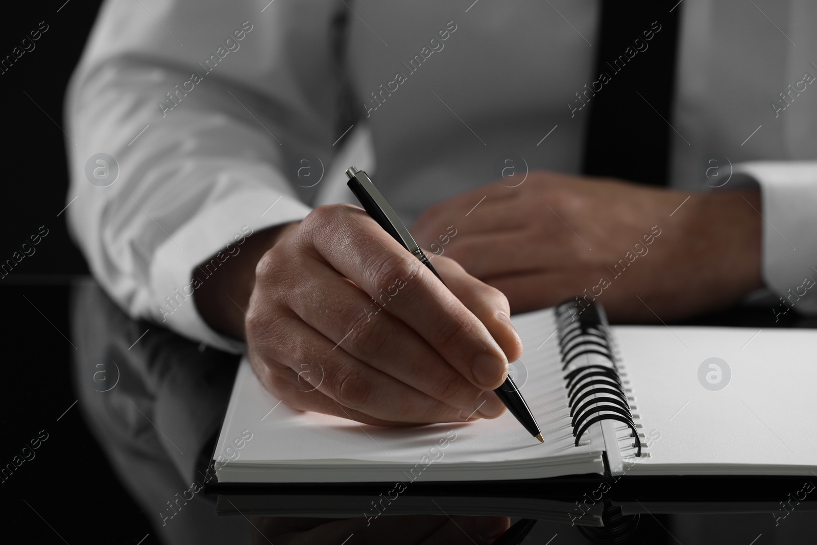 Photo of Man writing in notebook at black table, closeup