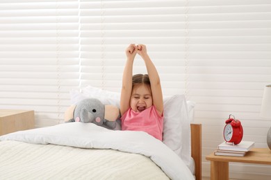 Photo of Cute little girl stretching and yawning in cosy bed