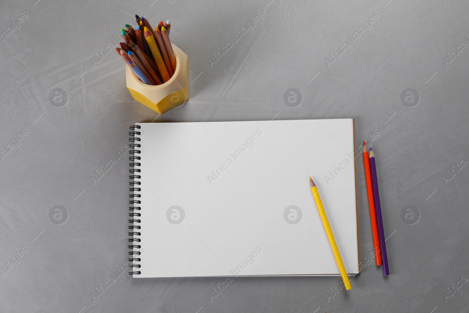 Photo of Empty sketchbook and colorful pencils on grey textured table, flat lay