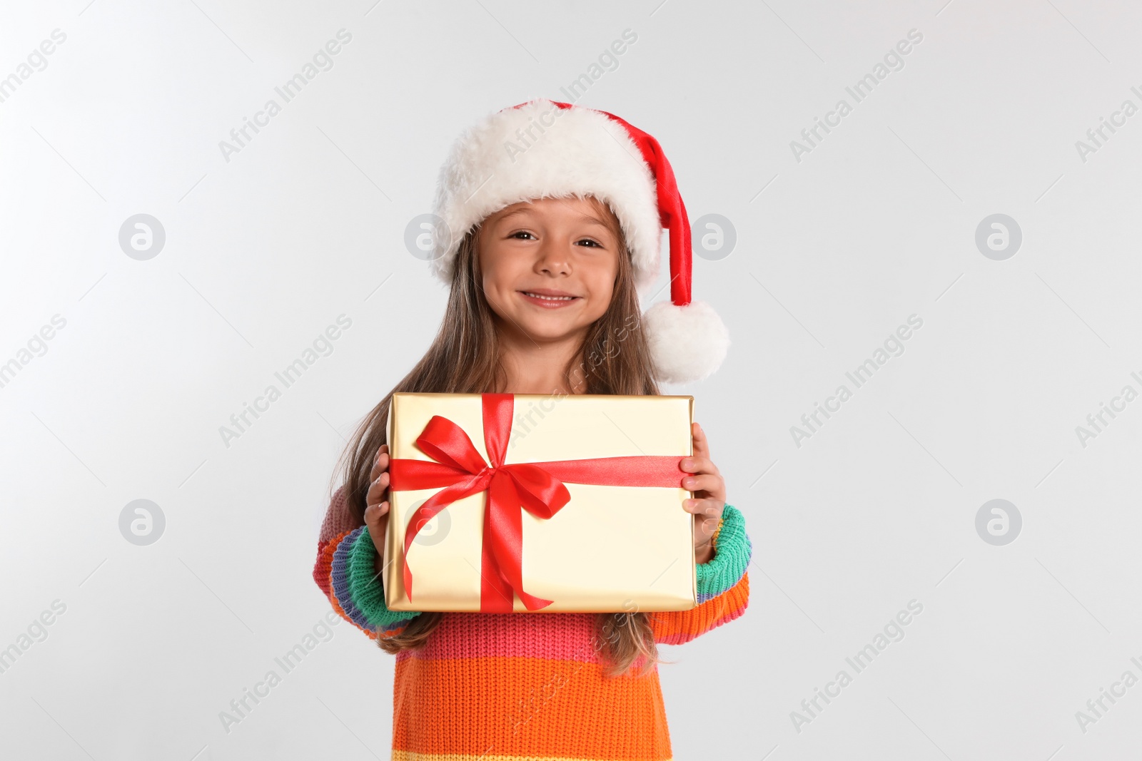 Photo of Happy little child in Santa hat with gift box on light grey background. Christmas celebration