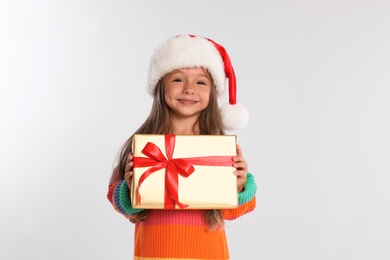 Photo of Happy little child in Santa hat with gift box on light grey background. Christmas celebration