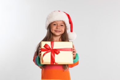 Happy little child in Santa hat with gift box on light grey background. Christmas celebration