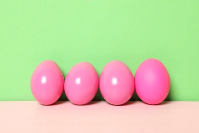 Photo of Easter eggs on pink wooden table against green background