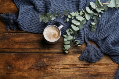 Flat lay composition with coffee and warm plaid on wooden table, space for text