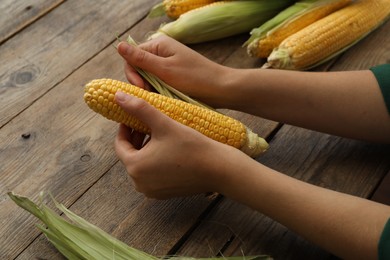 Photo of Woman husking corn cob at wooden table, closeup