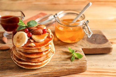 Stack of tasty pancakes with banana, berries, nuts and syrup on wooden board