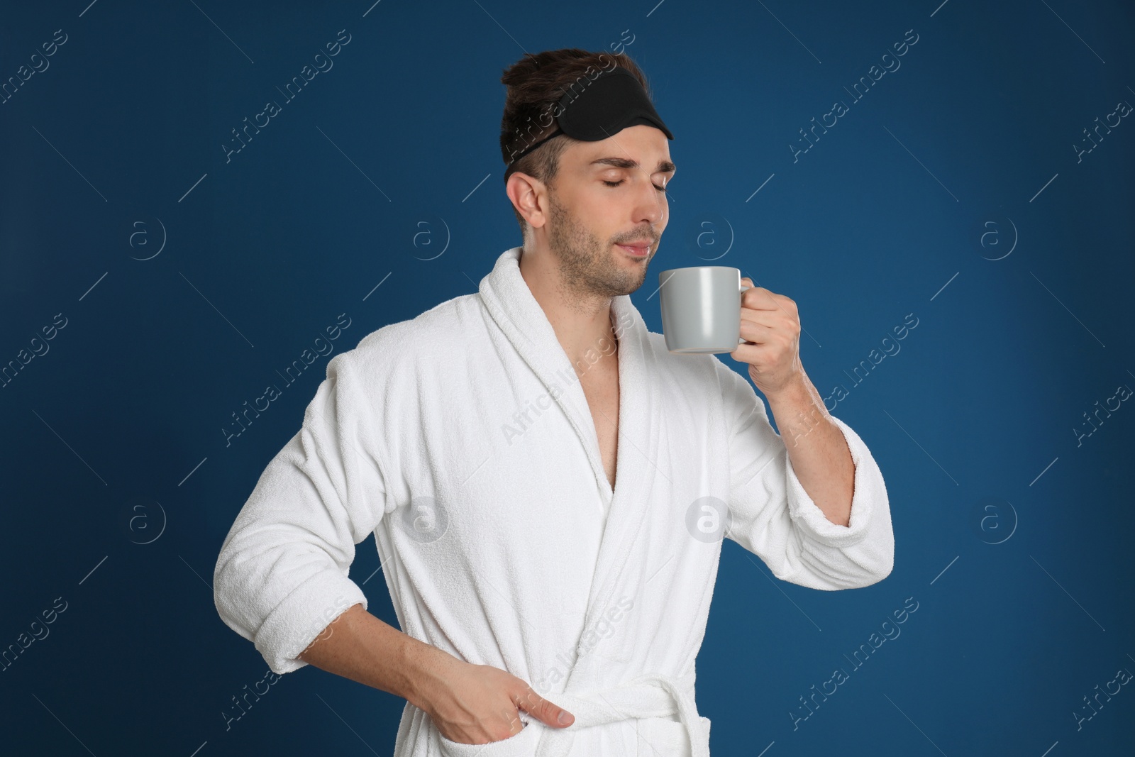 Photo of Young man in bathrobe with cup of coffee on blue background