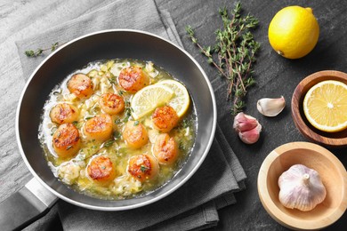 Photo of Delicious scallops with sauce in frying pan and ingredients on dark gray textured table, above view