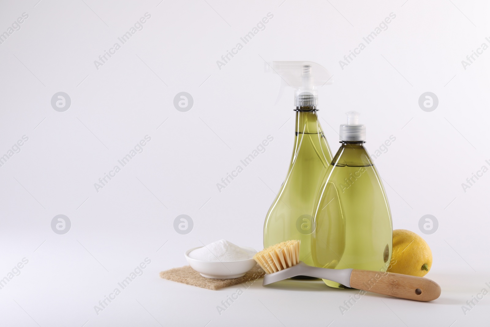 Photo of Bottles of cleaning product, brush, baking soda and lemon on white background