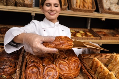 Baker putting fresh bun into paper bag in store