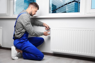 Photo of Professional plumber using pliers while preparing heating radiator for winter season in room