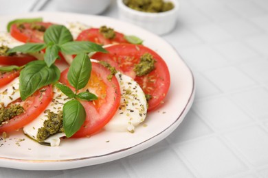 Plate of delicious Caprese salad with pesto sauce on white tiled table, closeup. Space for text