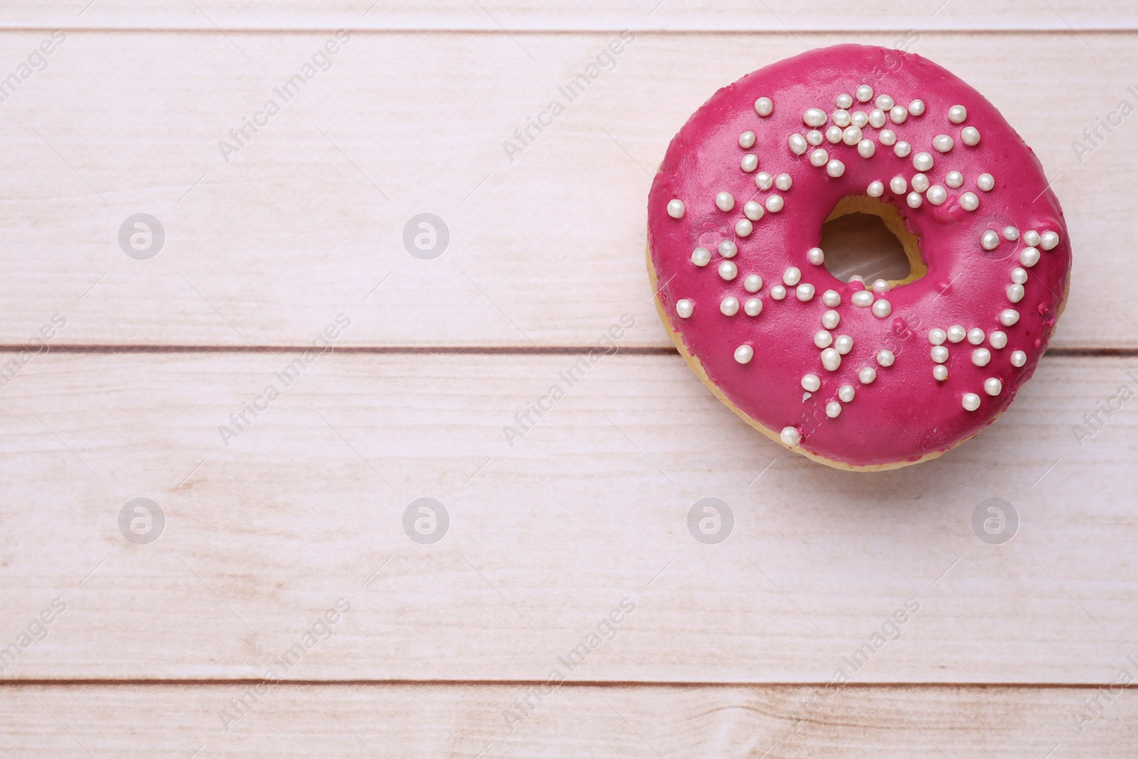 Photo of Tasty glazed donut decorated with sprinkles on white wooden table, top view. Space for text