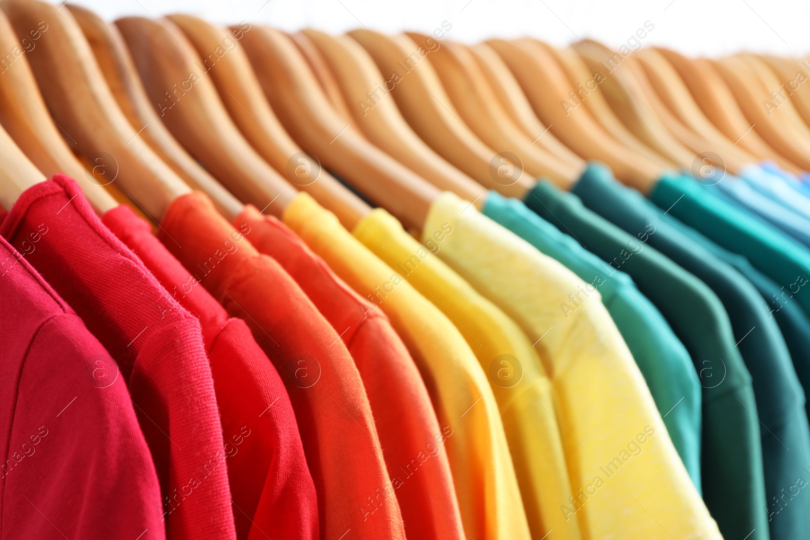 Photo of Hangers with bright clothes on light background, closeup