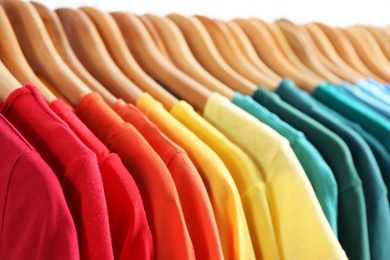 Hangers with bright clothes on light background, closeup