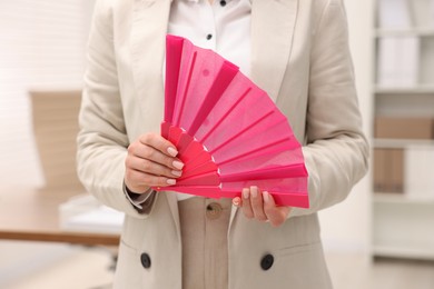 Photo of Businesswoman with pink hand fan in office, closeup
