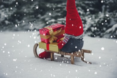 Wooden sleigh with Christmas gnome and gift boxes on snow outdoors