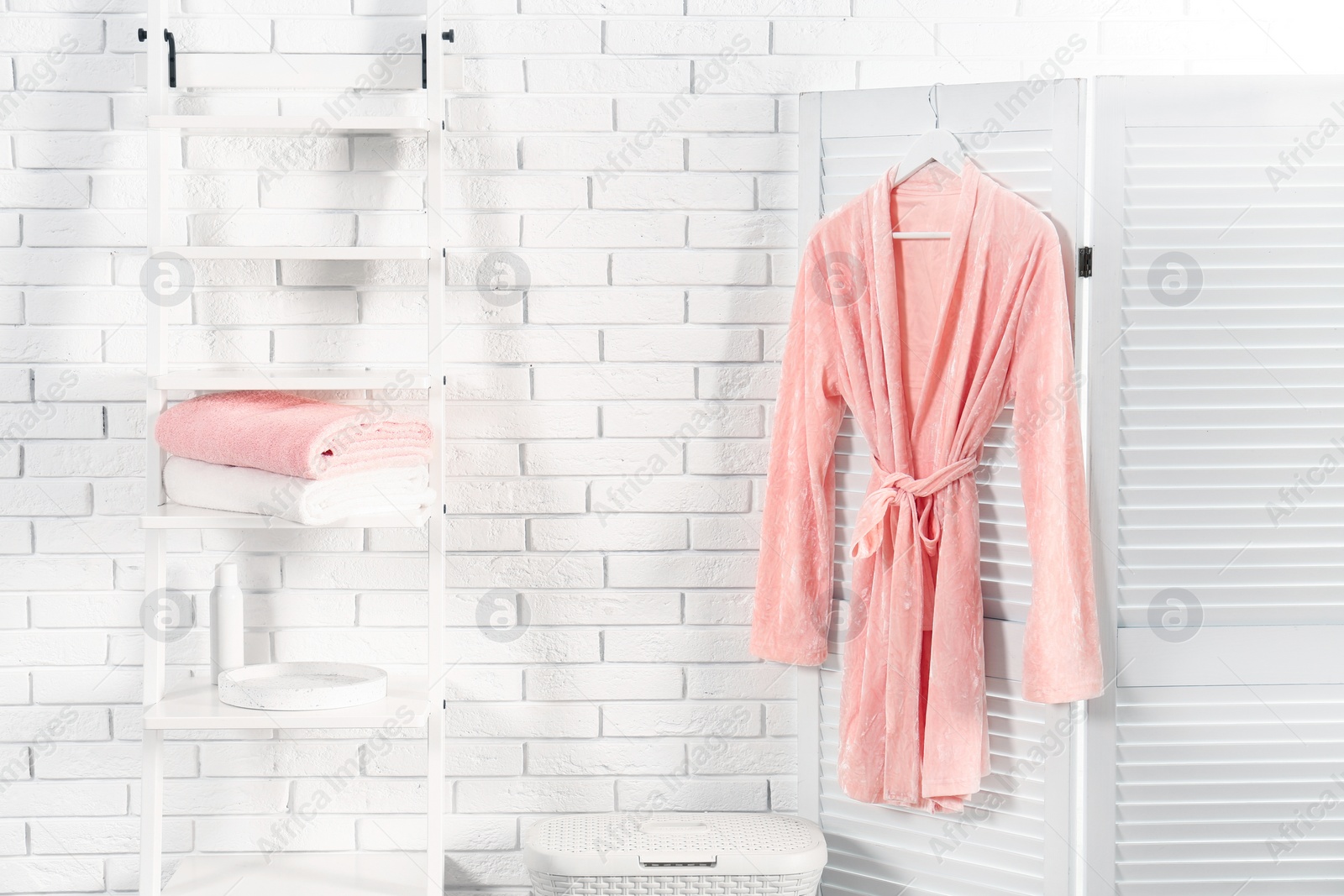 Photo of Shelving unit with clean towels and robe near brick wall