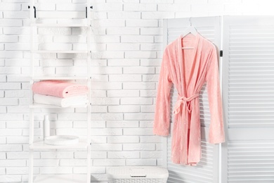 Shelving unit with clean towels and robe near brick wall