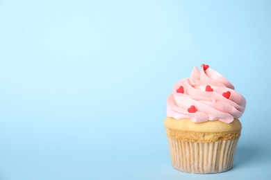 Photo of Tasty cupcake with heart shaped sprinkles on light blue background, space for text. Valentine's Day celebration