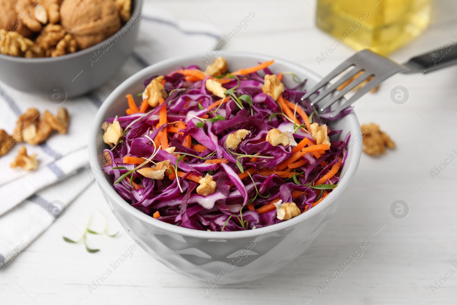 Photo of Eating tasty salad with red cabbage and walnuts at white wooden table, closeup
