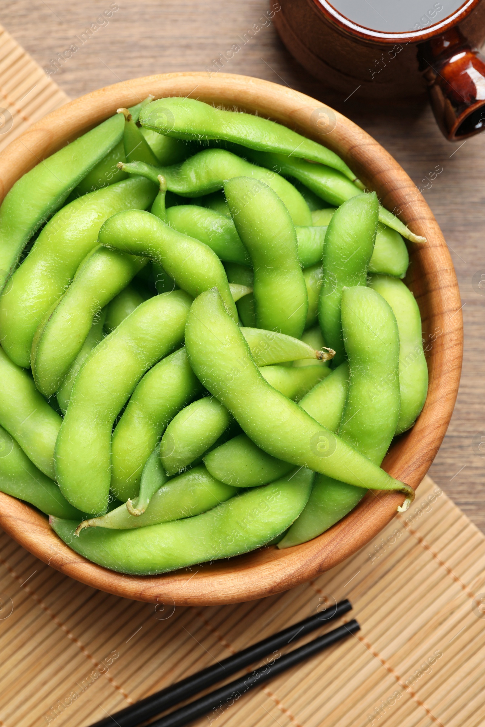 Photo of Green edamame beans in pods served with soy sauce on wooden table, flat lay