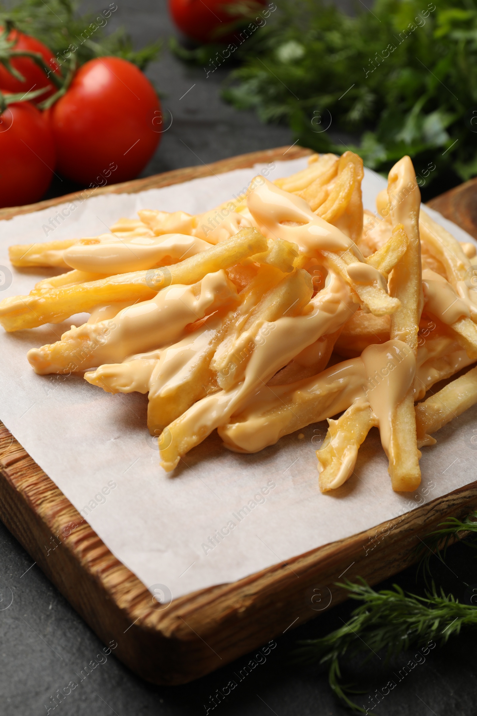 Photo of Delicious French fries with cheese sauce, tomatoes and dill on black table, closeup