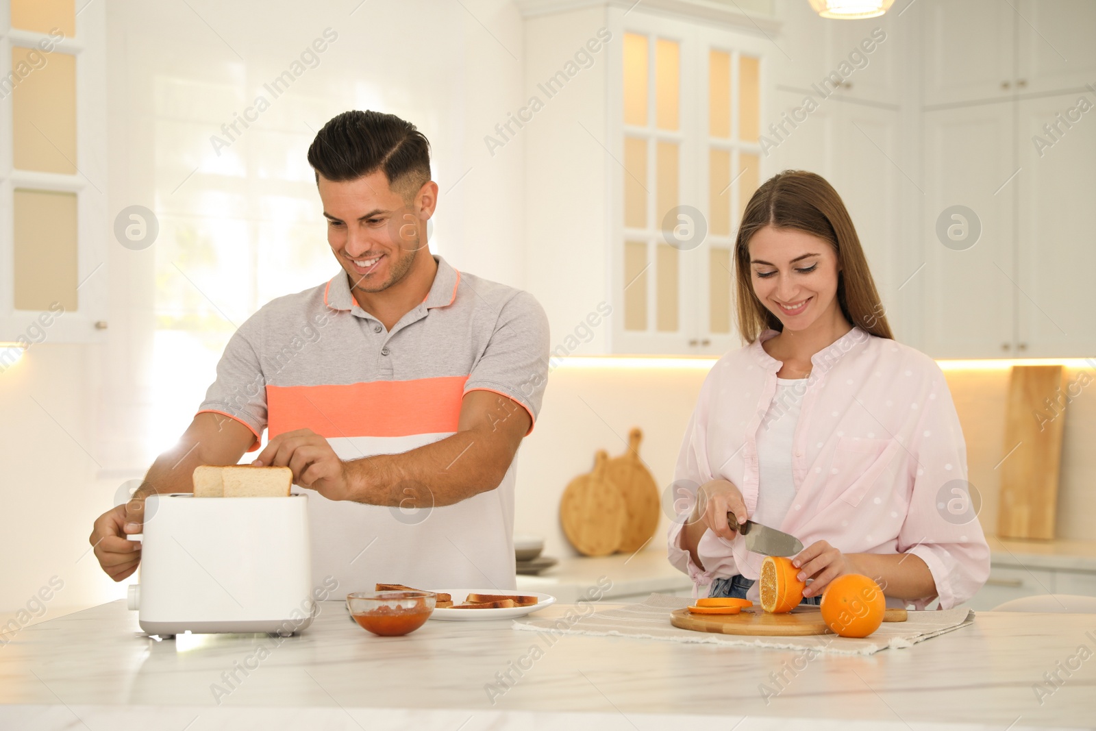 Photo of Happy couple preparing breakfast with toasted bread at table in kitchen