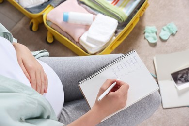 Photo of Pregnant woman preparing list of necessary items to bring into maternity hospital at home, top view