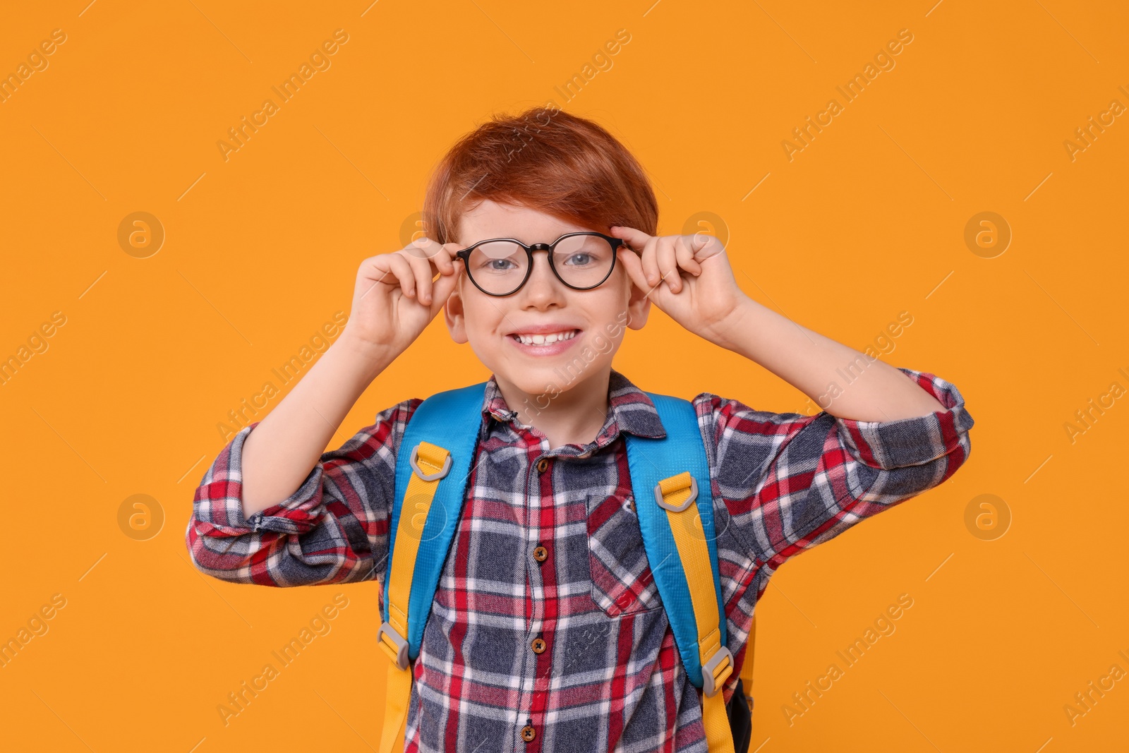 Photo of Happy schoolboy in glasses on orange background