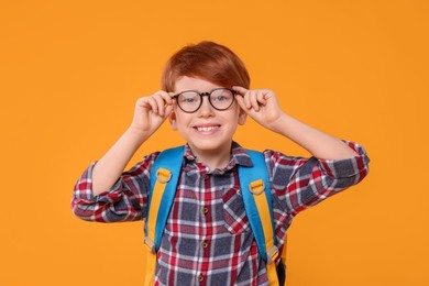 Photo of Happy schoolboy in glasses on orange background